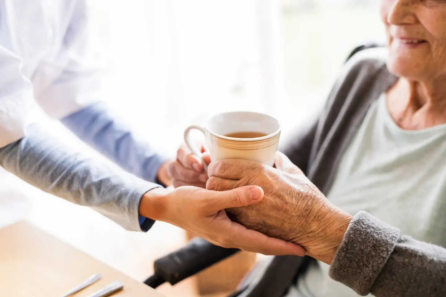 care visitor senior woman home visit nurse giving cup tea elderly woman sitting table close up