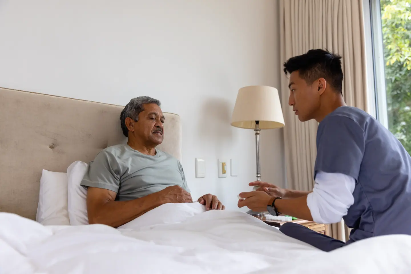 diverse male doctor senior male patient bed discussing home medical services check up home visit healthcare wellbeing senior lifestyle unaltered